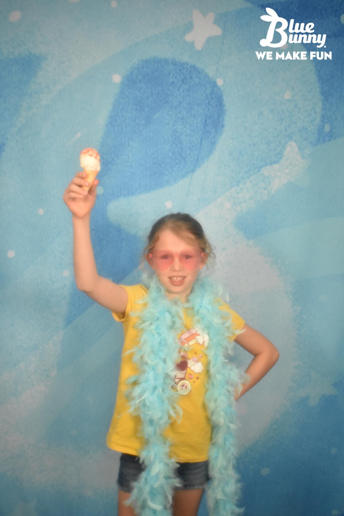 Girl with a blue boa holding up a mini swirl with pink heart glasses