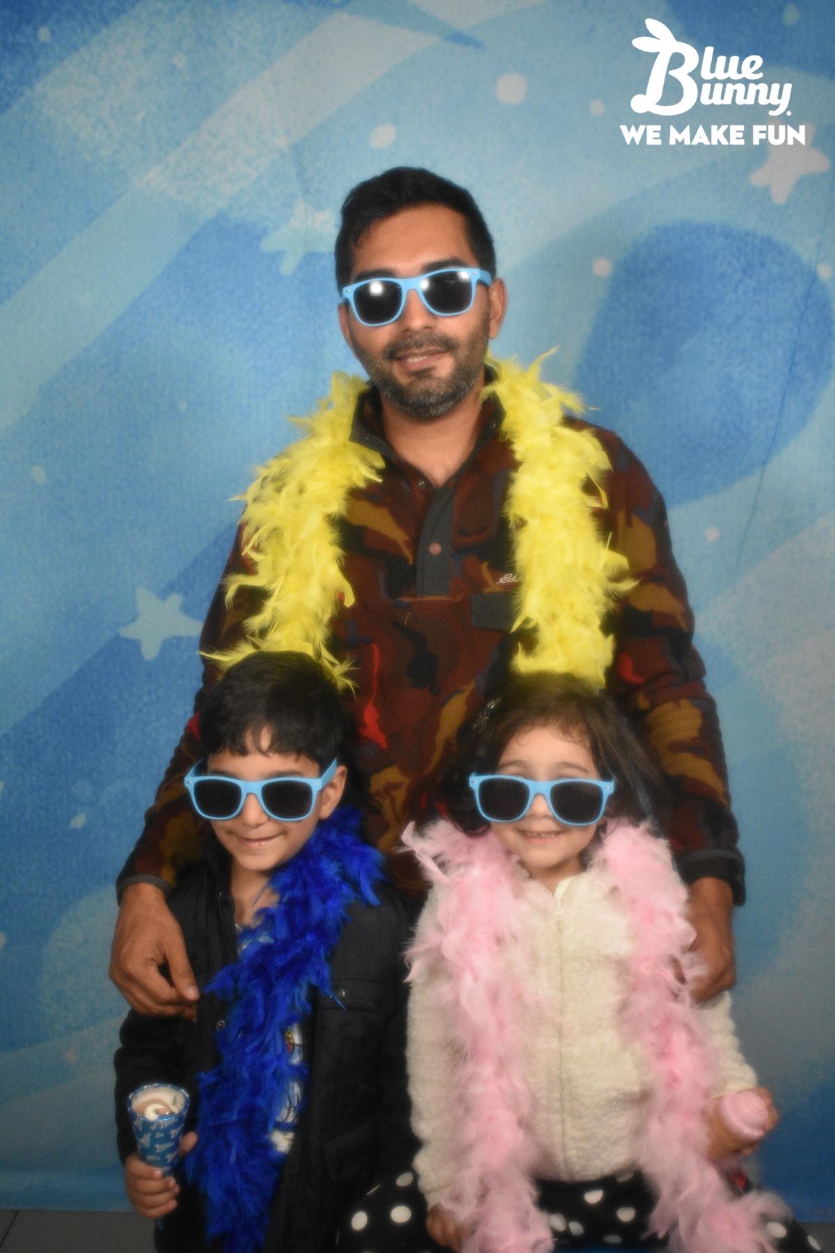 Dad with his son and daughter wearing sunglasses and boas. The sun is holding a twist cone.