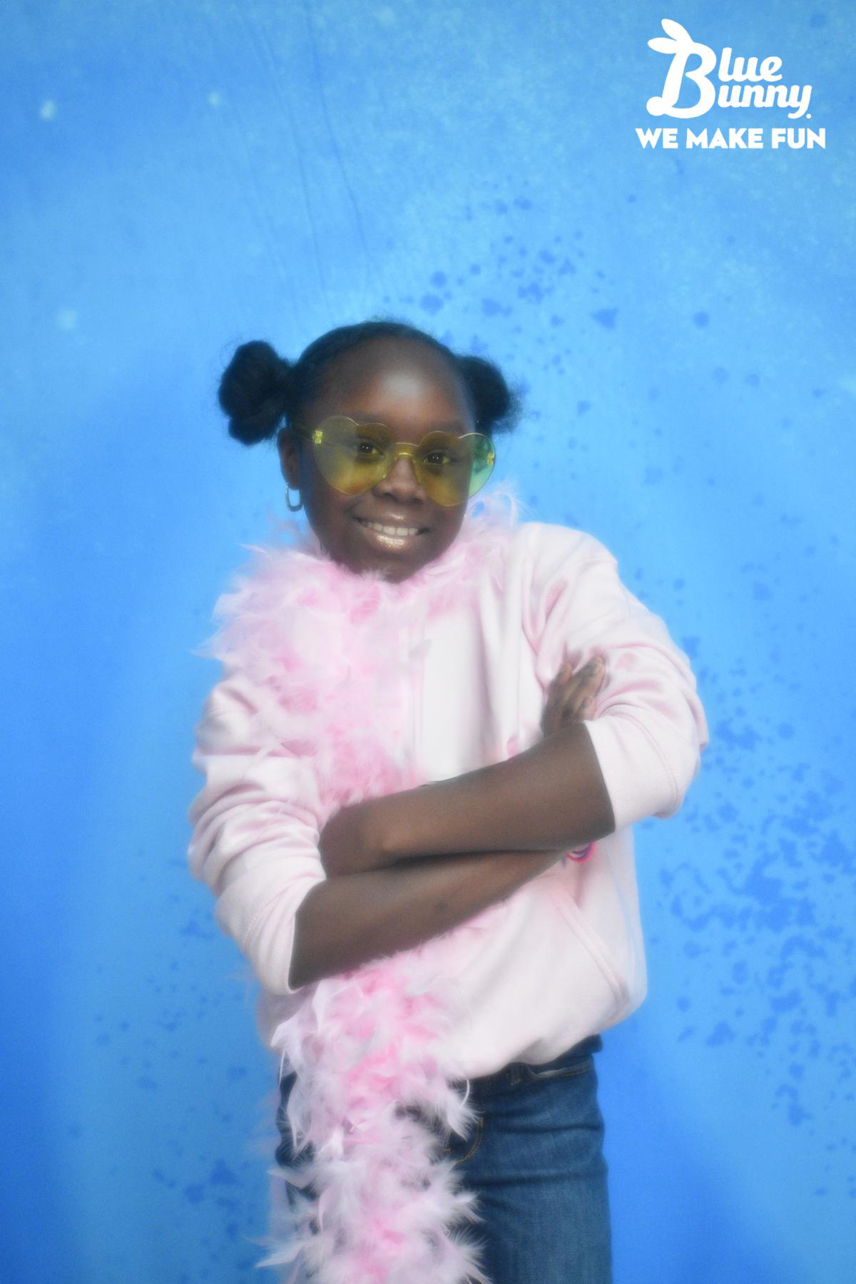 Young girl with her arms crossed with a pink boa and yellow heart sunglasses